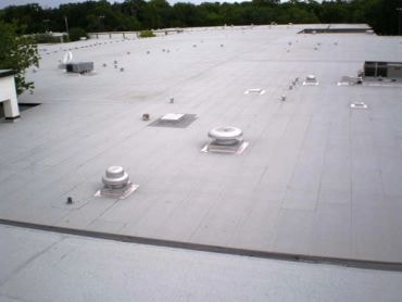 Worker applying white roof coating on commercial flat roof